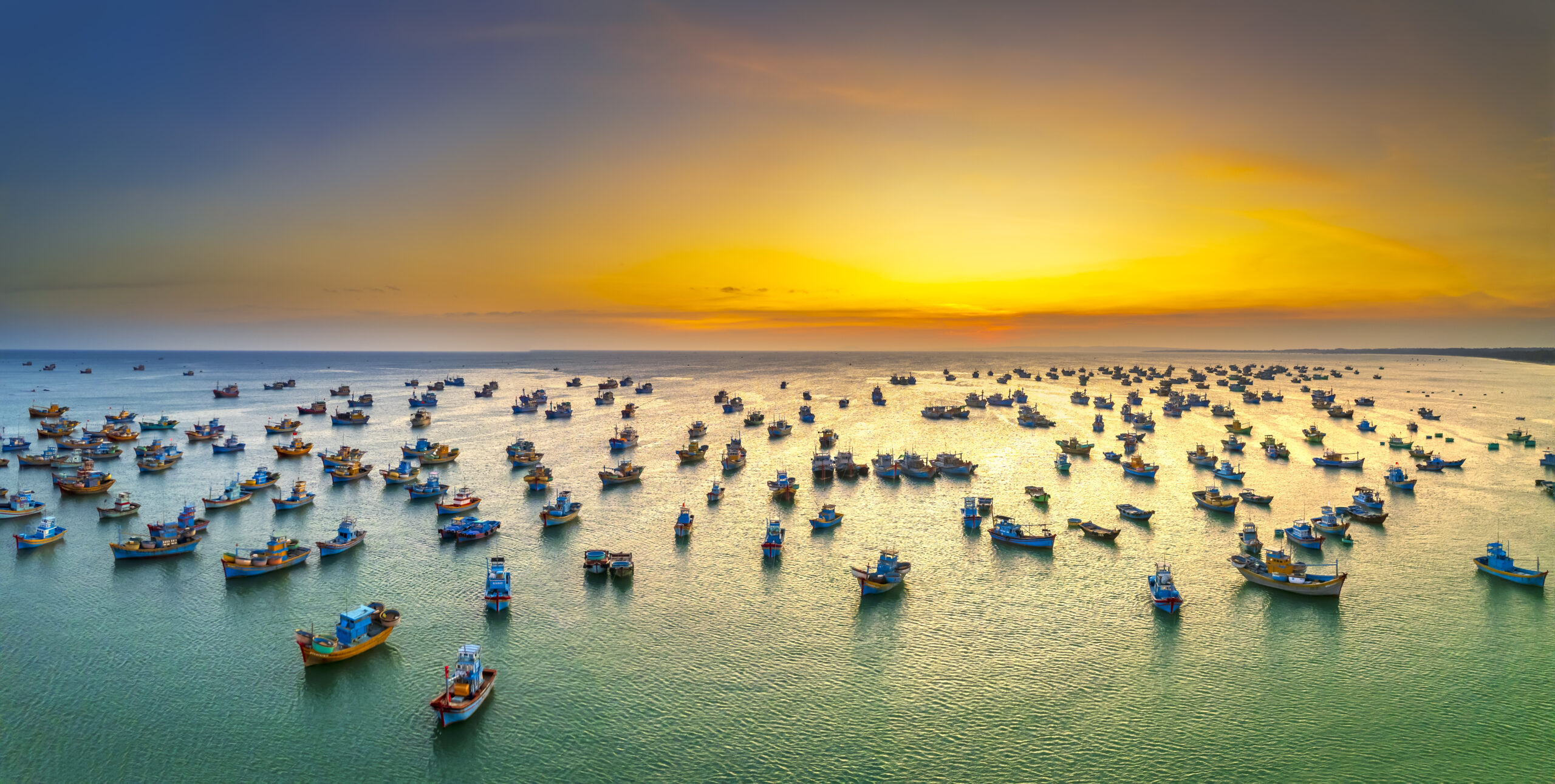 Many boats at sea with a colorful sky from setting sun.